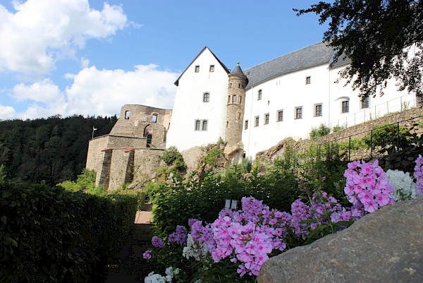 Schloss Lauenstein: weißes Gebäude auf Felsen, davor Garten mit Blumen