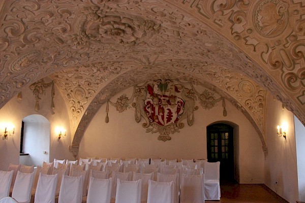 Der Wappensaal - Das Gewölbe des Saales ist mit einer üppigen Stuckdecke verziert. Die Rückwand ziert ein großes Allianzwappen aus Stuck. Es ist das Wappen der Schlossherren von Bünau und das Wappen der Familie von Bredow.
