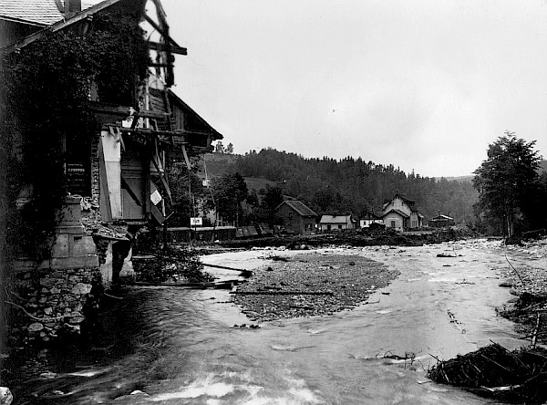 Bahnhof Lauenstein nach dem Hochwasser 1927, historische Schwarz-Weiß-Fotografie, links ein durch Flut zerstörtes Haus, in Bildmitte die Müglitz nach dem Hochwasser